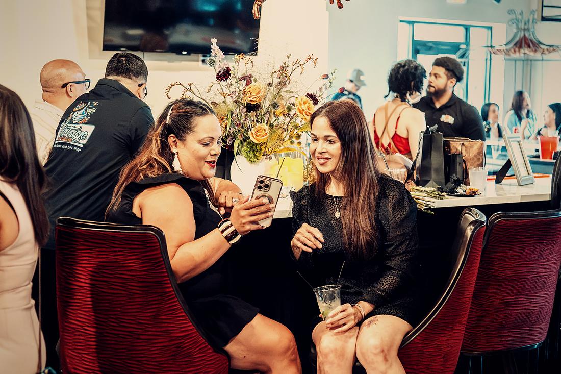 Two guests at a table in the red velvet chairs, flowers between them.