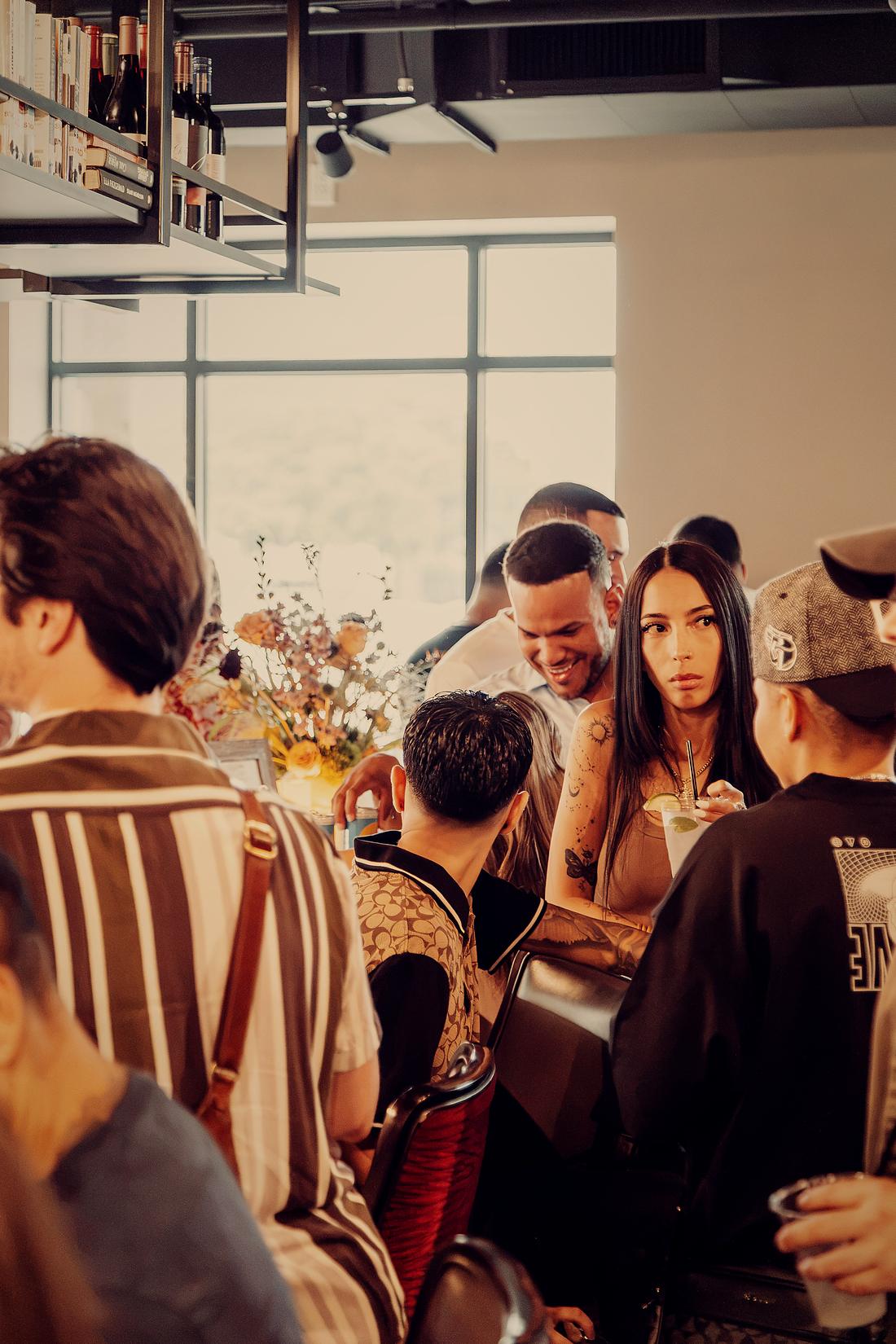 Guests leaning in together at a table, flowers behind them.